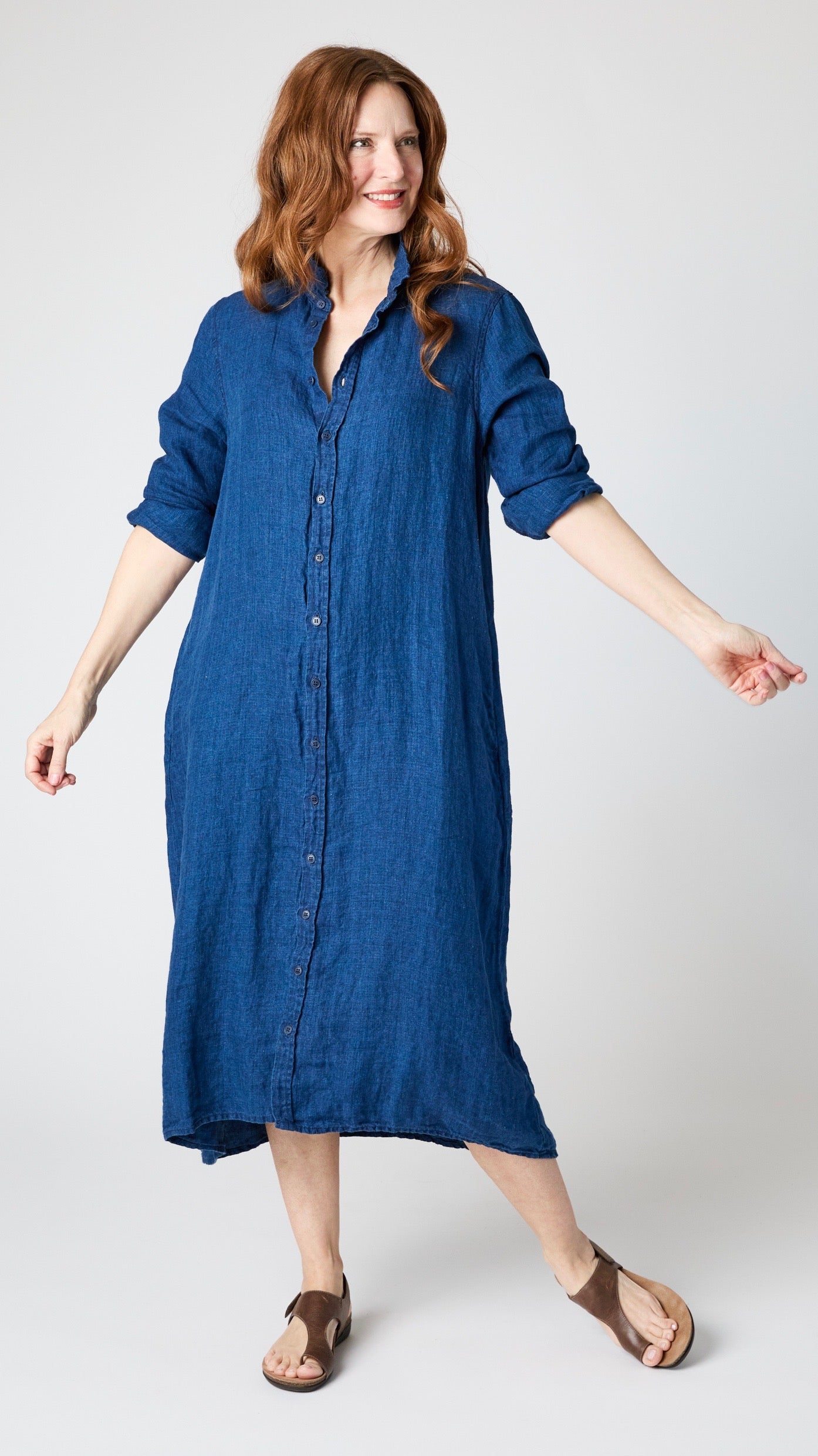 Model wearing indigo twill shirtdress with pointed collar and full length button-up panel, and brown leather sandals.