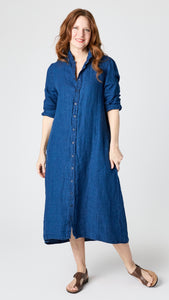 Model wearing indigo twill shirtdress with pointed collar and full length button-up panel, and brown leather sandals.