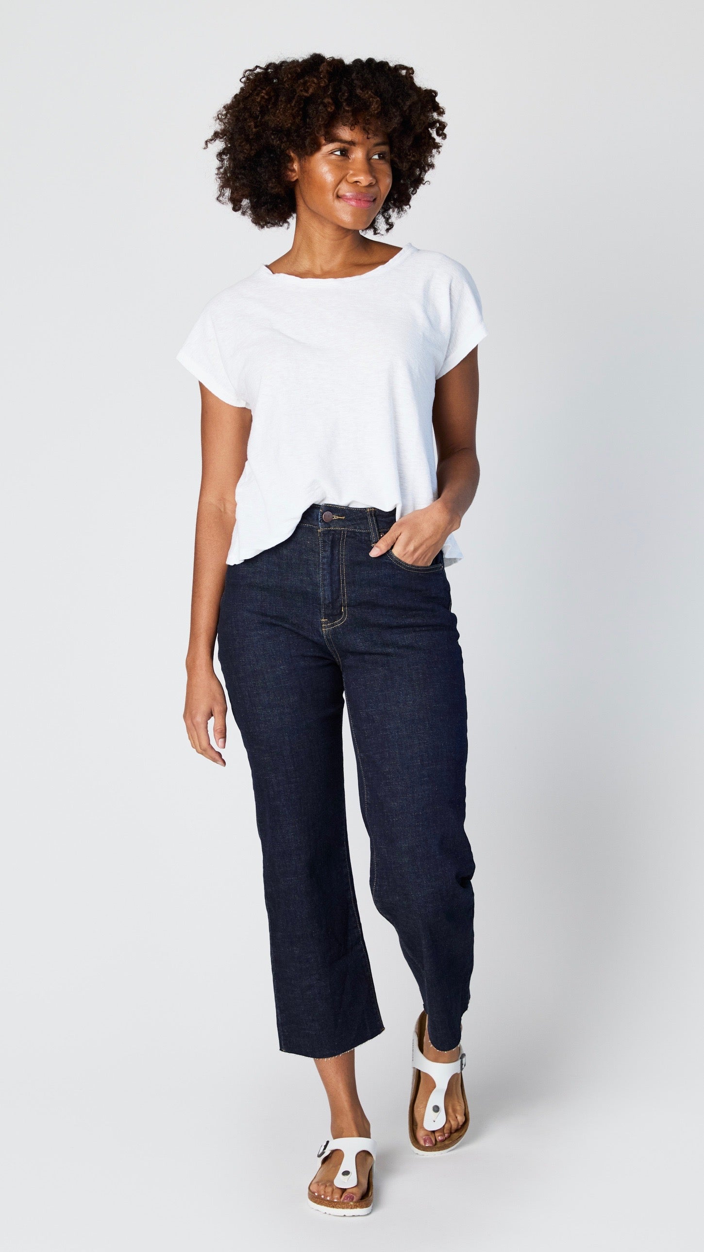 Model wearing dark-wash cropped wide leg jeans with raw hem, white cotton/jersey blend short sleeve tee, and white sandals.