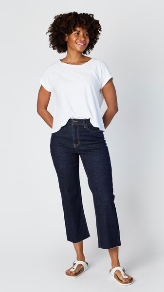 Model wearing dark-wash cropped wide leg jeans with raw hem, white cotton/jersey blend short sleeve tee, and white sandals.