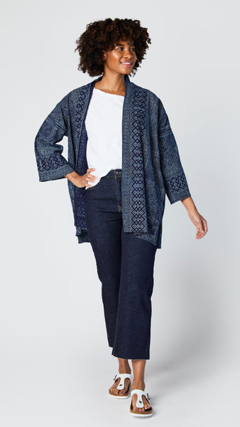 Model wearing dark-wash cropped wide leg jeans with raw hem, white cotton/jersey blend short sleeve tee, indigo batik kimono, and white sandals.