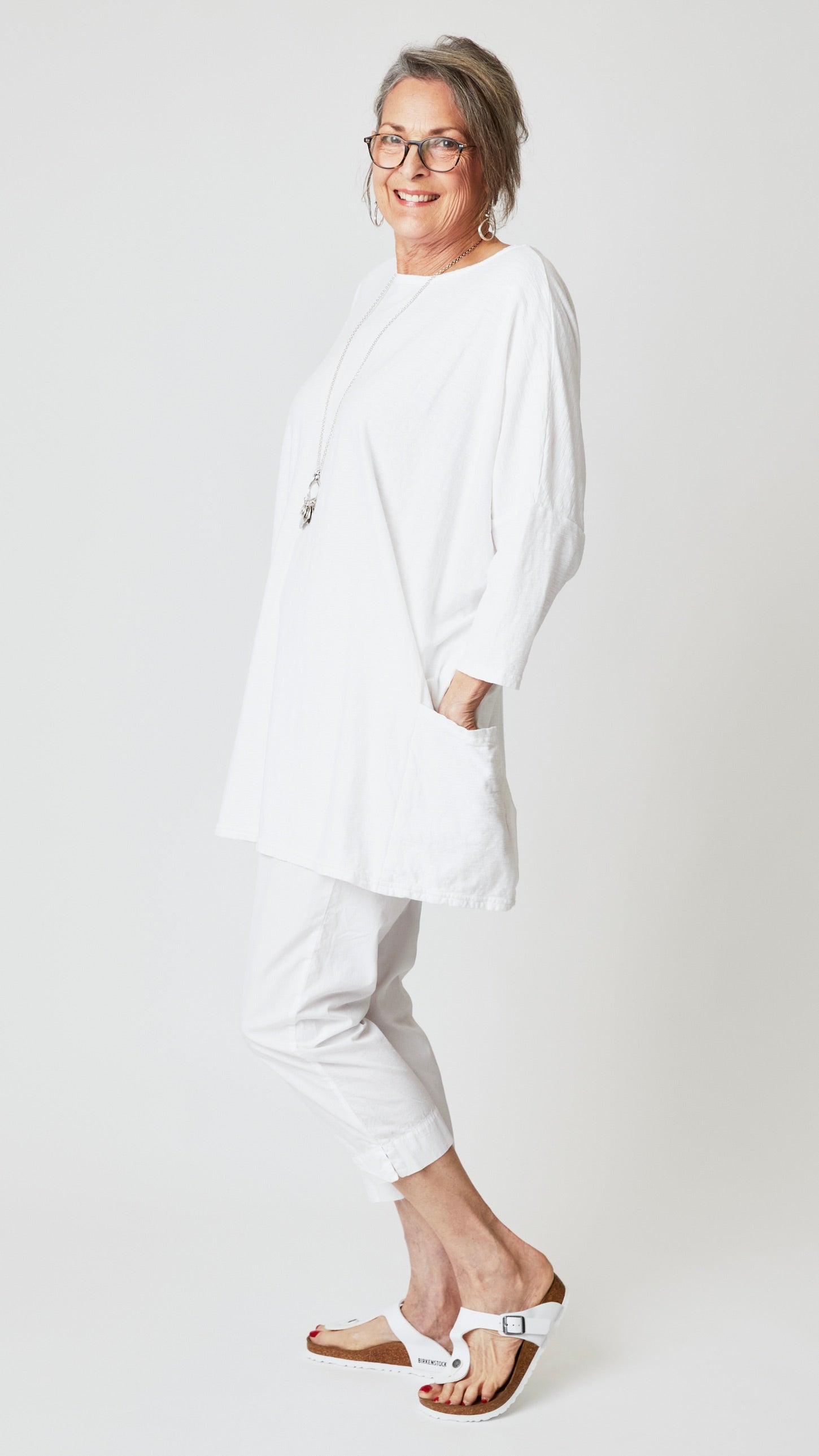 Model wearing white one size roomy two pocket tunic top, white tapered cropped pant in organic poplin, and white sandals.