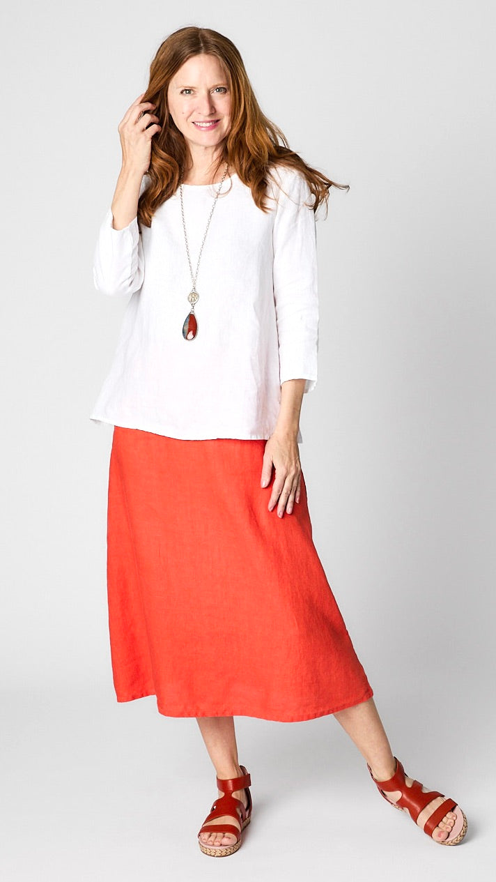 Model wearing white linen 3/4 sleeve shirt with A-line silhouette, “tabasco” orange A-Line Linen skirt, coin pendant necklace, and leather sandals.
