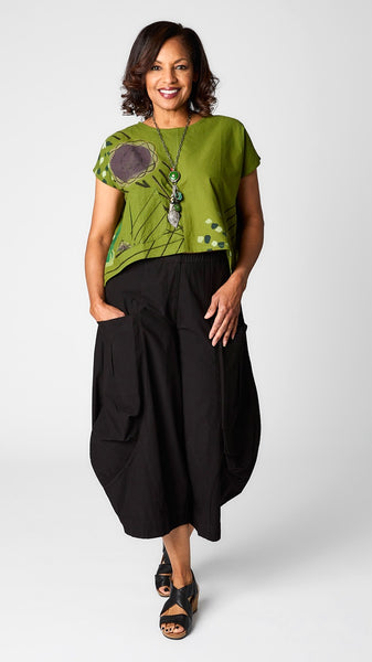 Model wearing grass green batik printed short sleeve top with curved cropped hemline over black cropped double pocket pant in tencel cotton.