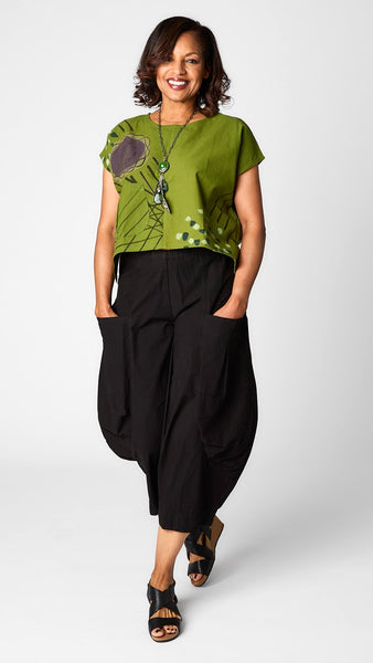 Model wearing grass green batik printed short sleeve top with curved cropped hemline over black cropped double pocket pant in tencel cotton.