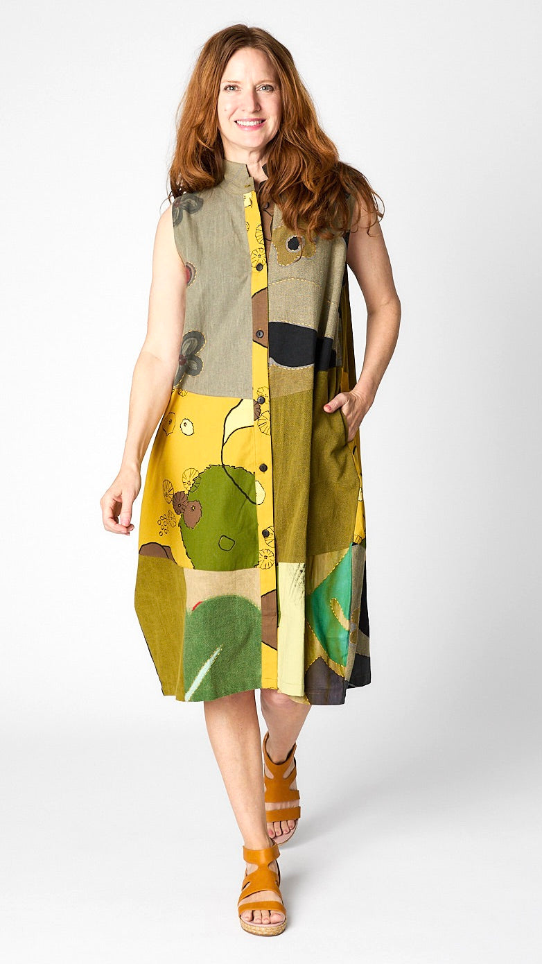 Model wearing “mustard” front button-opening sleeveless dress/vest with bubble silhouette and raised collar, and yellow leather sandals.