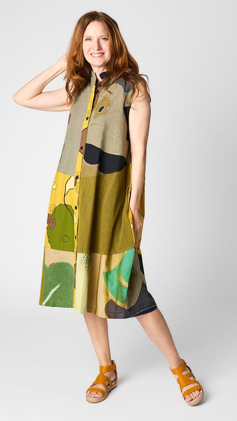 Model wearing “mustard” front button-opening sleeveless dress/vest with bubble silhouette and raised collar, and yellow leather sandals.