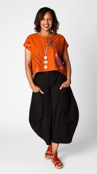 Model wearing orange batik printed short sleeve top with curved cropped hemline over black cropped double pocket pant in tencel cotton.