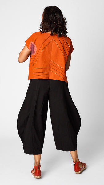 Model wearing orange batik printed short sleeve top with curved cropped hemline over black cropped double pocket pant in tencel cotton.