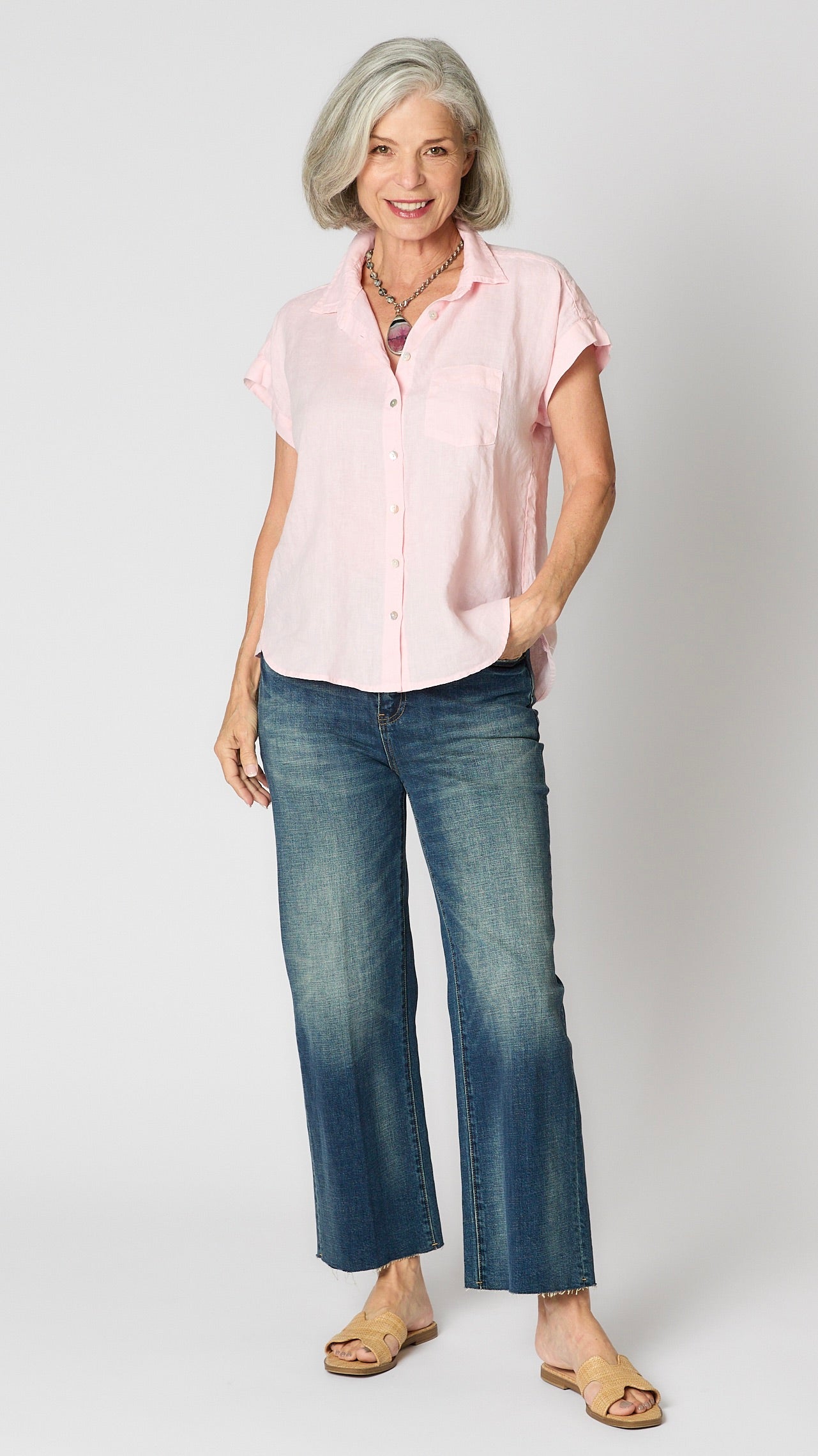 Model wearing pink linen short sleeve button-up shirt, vintage wash cropped jeans, and beige sandals.