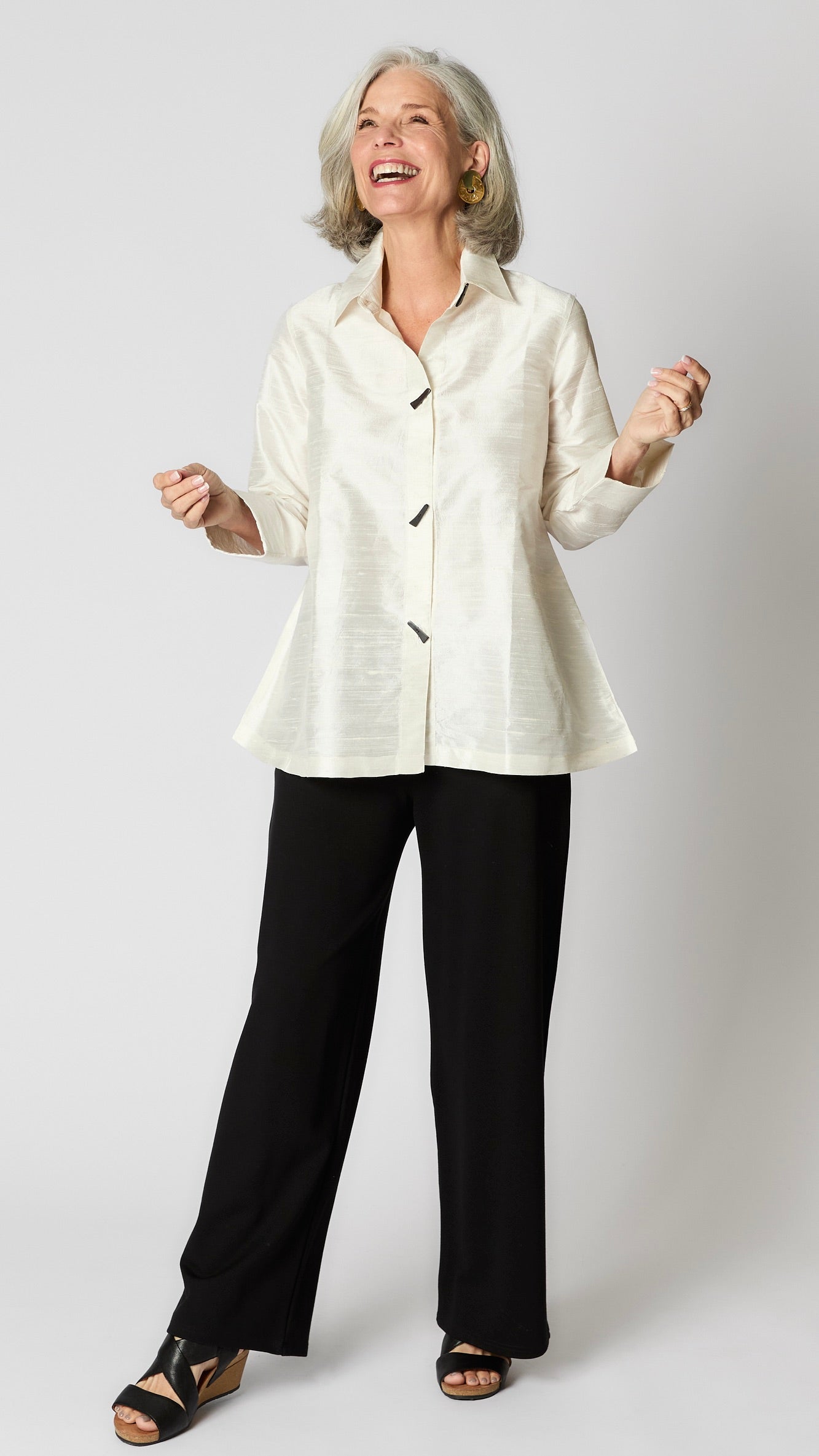 Model wearing ivory raw silk button-up blouse with black horn buttons and 3/4 sleeves, black wideleg trousers, and black wedge sandals.