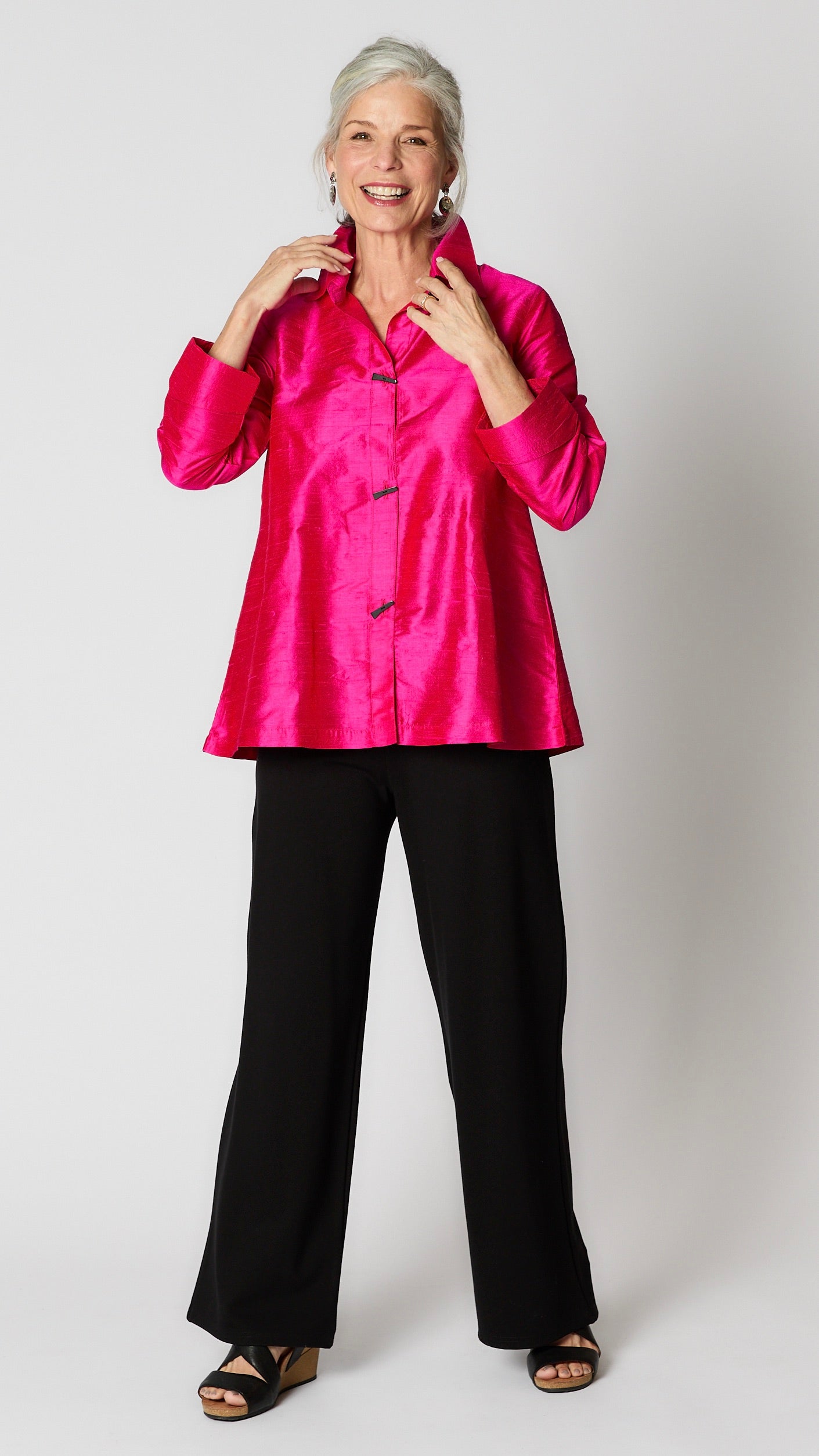 Model wearing fuchsia raw silk button-up blouse with black horn buttons and 3/4 sleeves, black wideleg trousers, and black wedge sandals.