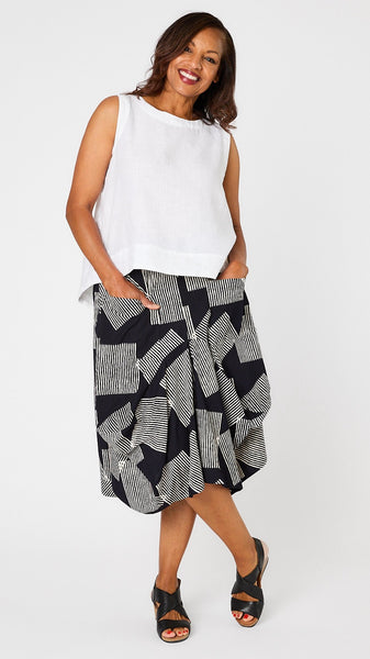 Model wearing white linen hi-lo tank top, black and white geometric patterned skirt with gathered panels and jersey waistband, and black leather sandals.