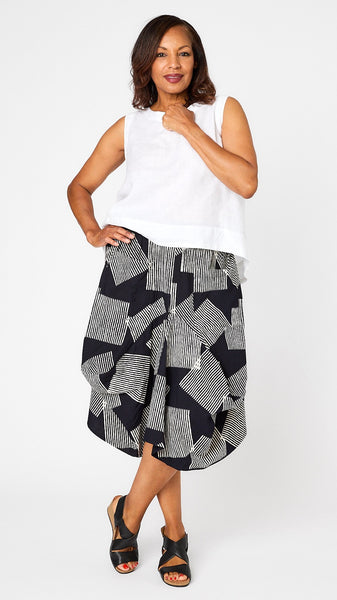 Model wearing white linen hi-lo tank top, black and white geometric patterned skirt with gathered panels and jersey waistband, and black leather sandals.