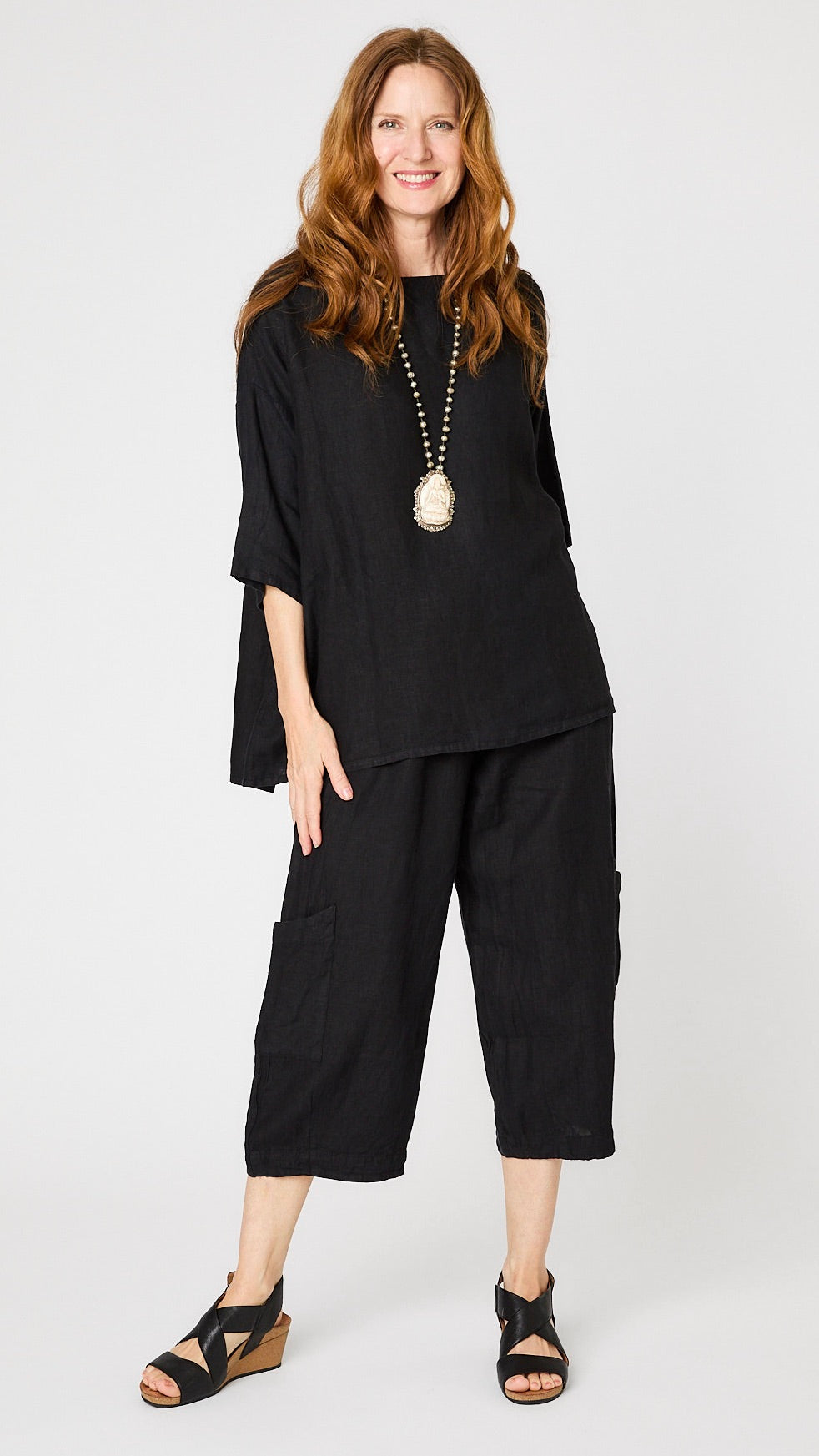 Model wearing black linen boatneck top with 3/4 sleeves and generous hemline, black cropped linen pants with patch pockets, and black sandals.