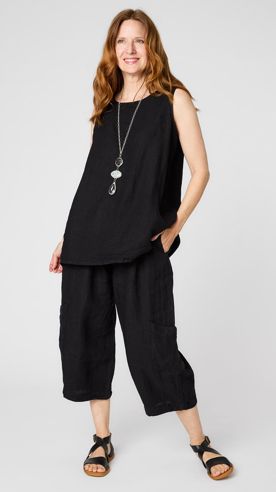 Model wearing black linen tank with relaxed fit over black cropped linen pants with ankle darts and patch pockets, and black leather sandals.