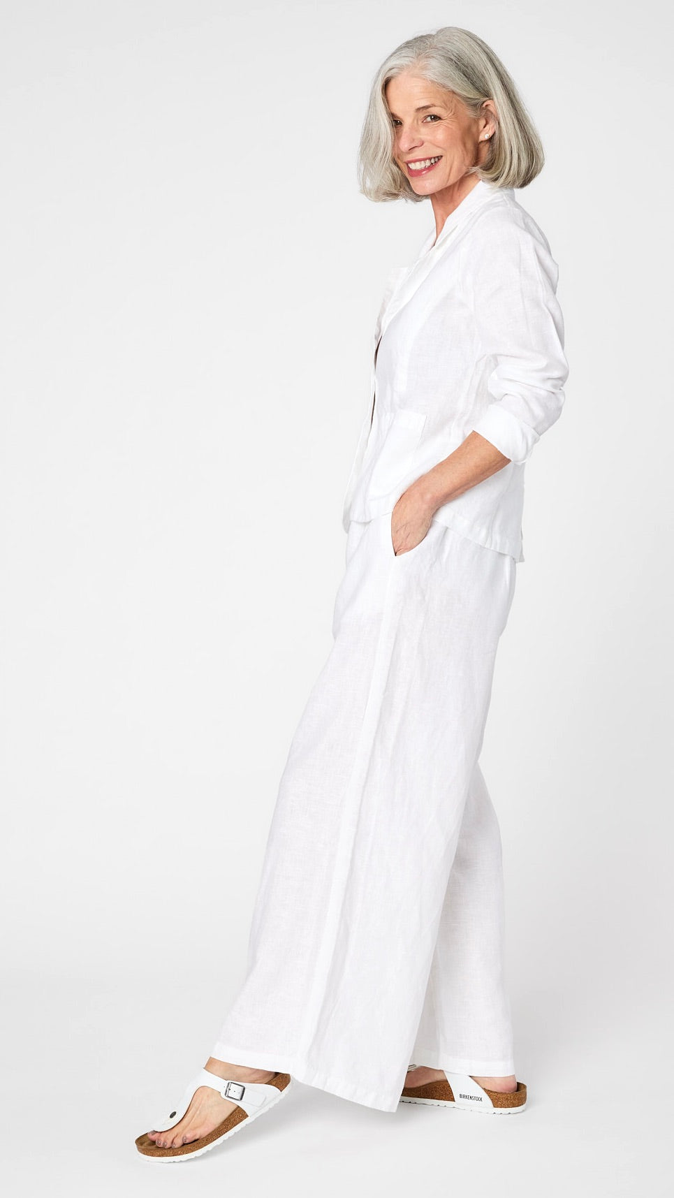 Model wearing white linen blazer over white, high waisted, wide leg linen pants with white sandals.