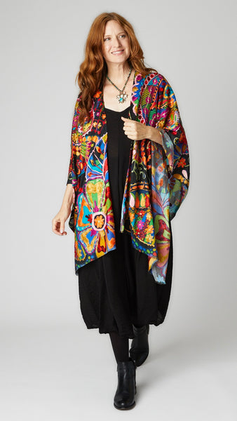 Model wearing multicolor/rainbow ruana with black background over black easy romper and black leather boots.