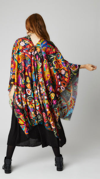 Model wearing multicolor/rainbow ruana with black background over black easy romper and black leather boots.