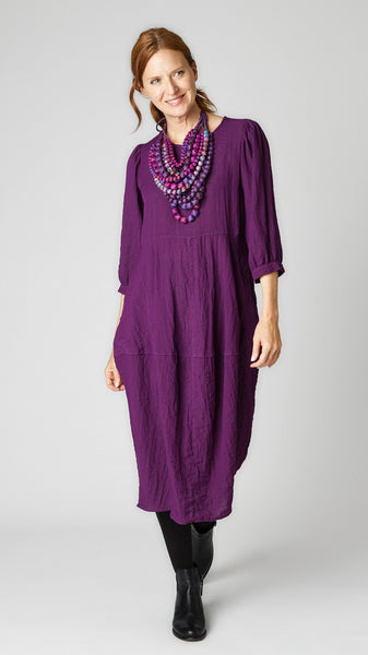 Model wearing mulberry mid-calf length rayon dress with black leggings and black leather boots. Dress has scoop neck, 3/4 sleeves, side seam pockets and slight tulip silhouette.