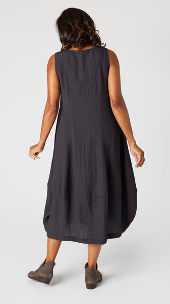 Model wearing "black pearl" sleeveless rayon dress with tulip hemline and round neck, beaded necklace with bone pendant, and gray suede boots.