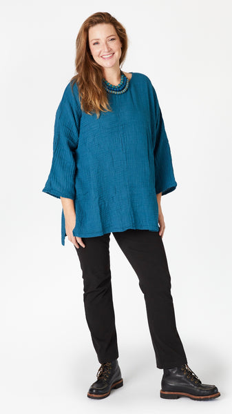 Model wearing teal 3/4 sleeve, split hem, flowy high-low tunic in double cotton, with beaded leather necklace, black straight leg jeans, and black lace-up leather boots.