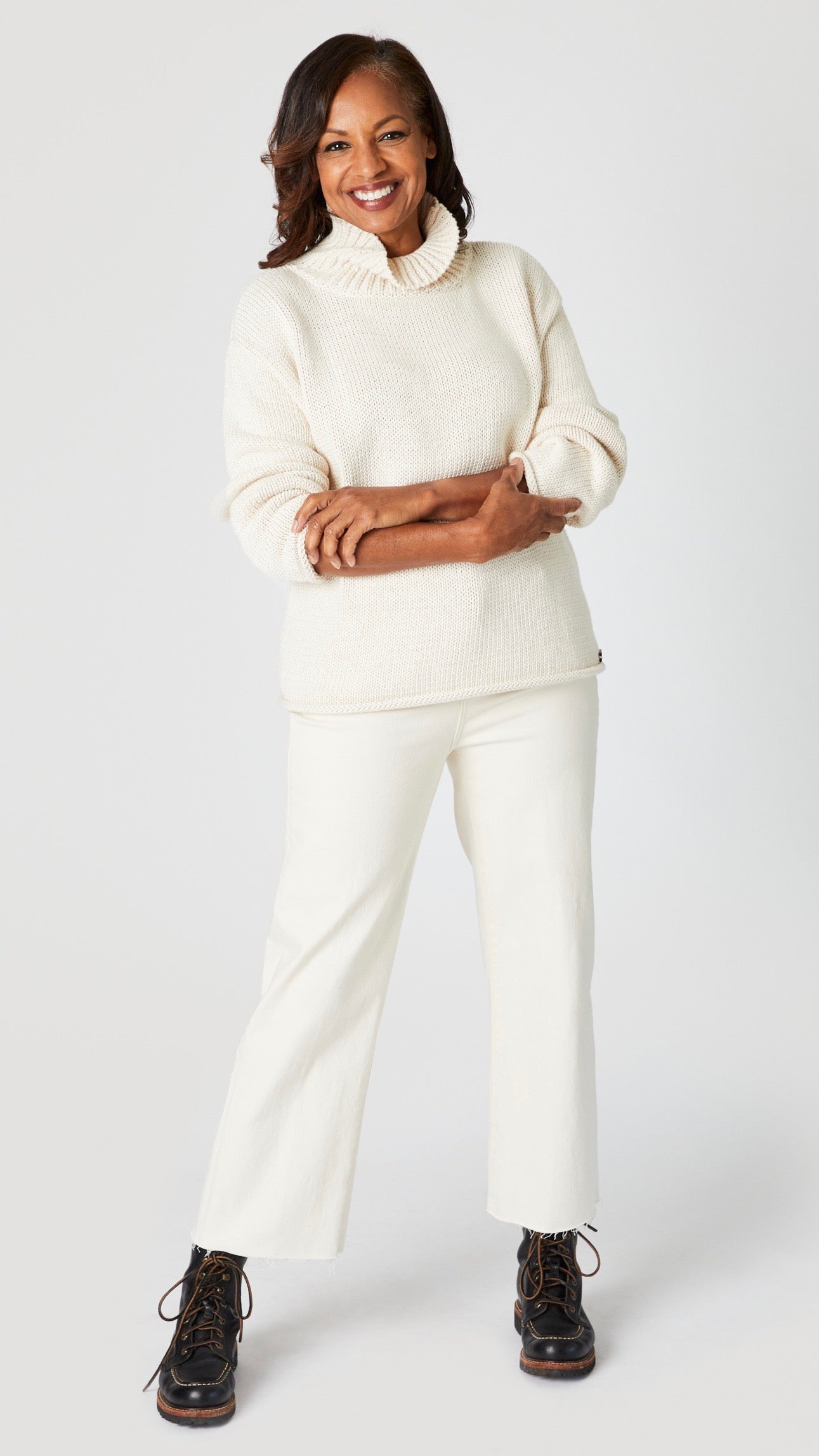 Model wearing hand knit cotton turtleneck sweater, and wide leg ankle length denim jeans with raw hem in ecru.