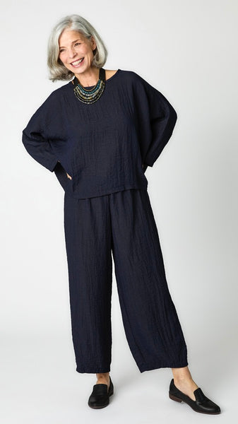 Model wearing cropped ink rayon top with high round neckline, dropped shoulders and ¾ sleeves, ink cropped dart pants, and black loafers.