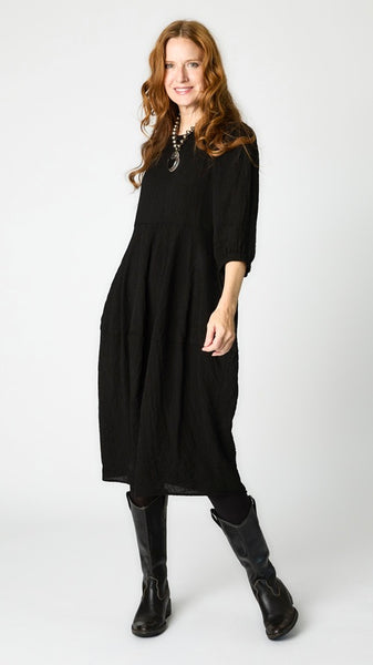Model wearing black rayon dress with scoop neck, 3/4 sleeves, and tulip hemline, with black leather boots.