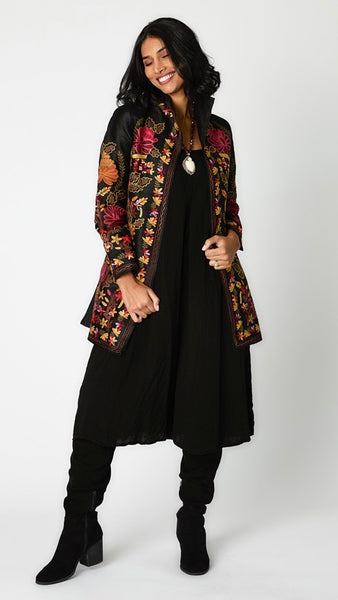 Model wearing black silk jacket with brown, rusty red & orange embroidery over black rayon romper and black suede boots.