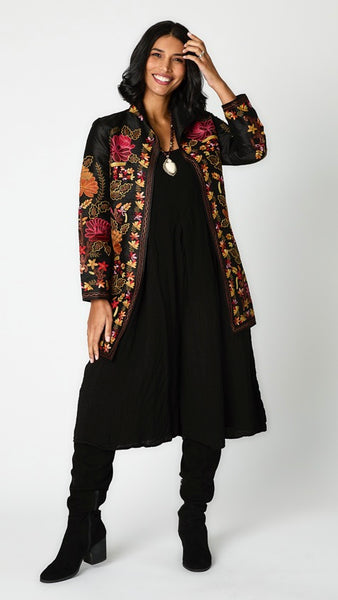 Model wearing black silk jacket with brown, rusty red & orange embroidery over black rayon romper and black suede boots.
