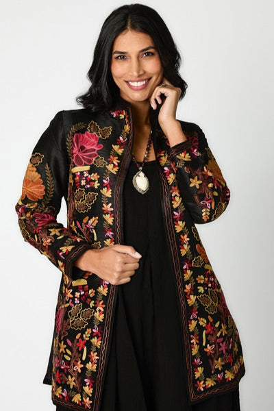 woman modeling womens clothing against a white background. she is wearing a black jumpsuit and embroidered elegant chic jacket