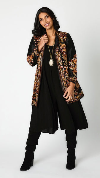 Model wearing black silk jacket with brown toned embroidery over black rayon romper and black suede boots.