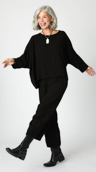 Model wearing black cropped one size top in travel weight rayon with black cropped pants with ankle darts and black leather boots.