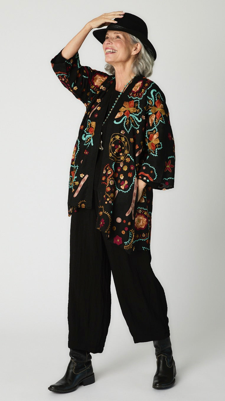 Model wearing black cotton kimono style jacket with turquoise and orange embroidery, black cropped top and black cropped dart pant in rayon with black leather boots.