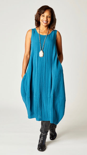 Model wearing "rainforest" sleeveless rayon dress with tulip hemline and round neck, beaded necklace with bone pendant, and black leather boots.