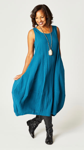 Model wearing "rainforest" sleeveless rayon dress with tulip hemline and round neck, beaded necklace with bone pendant, and black leather boots.