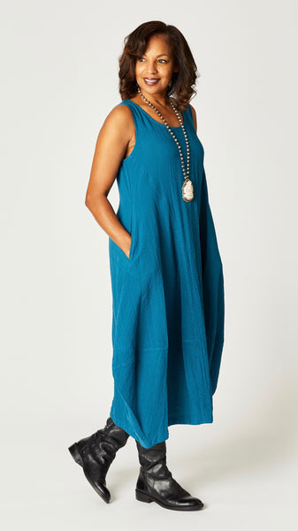 Model wearing "rainforest" sleeveless rayon dress with tulip hemline and round neck, beaded necklace with bone pendant, and black leather boots.