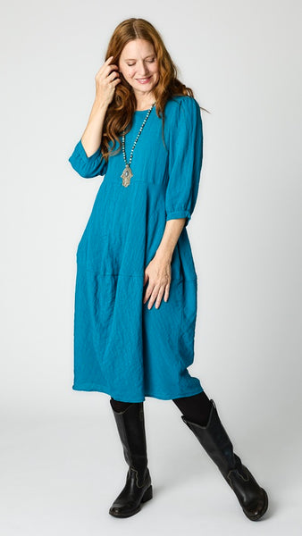 Model wearing deep sea mid-calf length rayon dress with black leggings and black leather boots. Dress has scoop neck, 3/4 sleeves, side seam pockets and slight tulip silhouette.