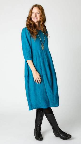 Model wearing deep sea mid-calf length rayon dress with black leggings and black leather boots. Dress has scoop neck, 3/4 sleeves, side seam pockets and slight tulip silhouette.