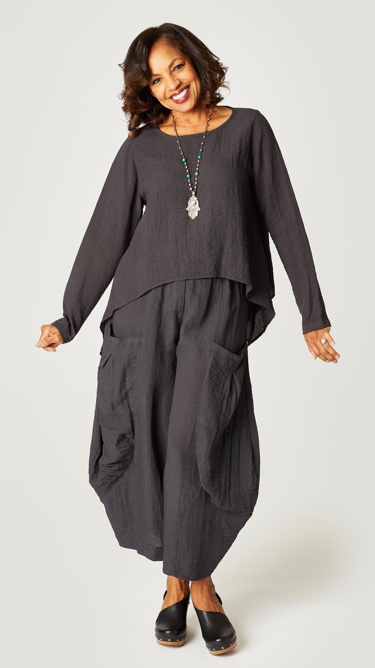 Model wearing black pearl long sleeve cropped top with A-line silhouette, black pearl double pocket pant, and hamsa pendant necklace.