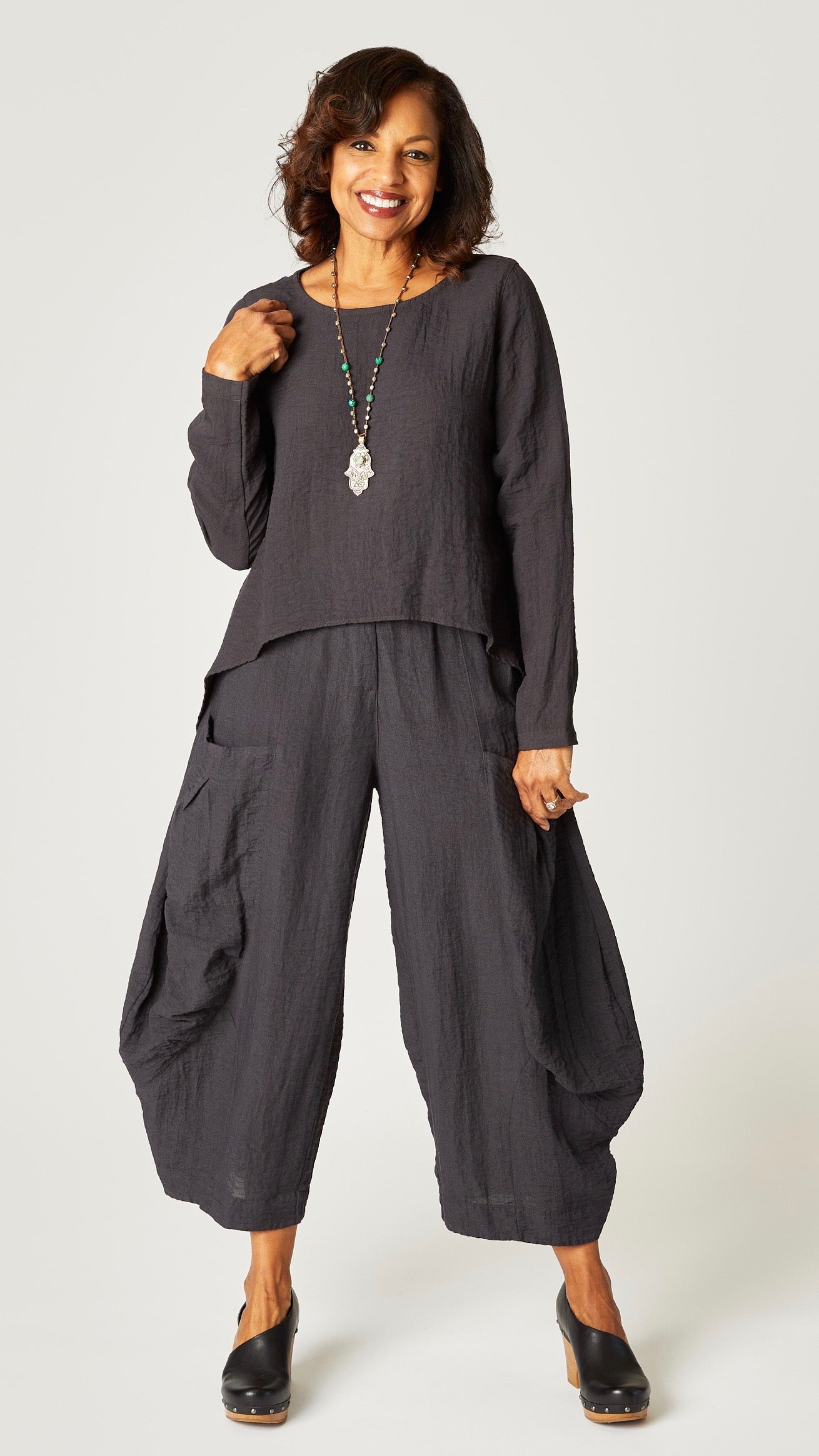Model wearing black pearl long sleeve cropped top with A-line silhouette, black pearl double pocket pant, and hamsa pendant necklace.