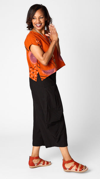 Model wearing orange batik printed short sleeve top with curved cropped hemline over black cropped double pocket pant in tencel cotton.