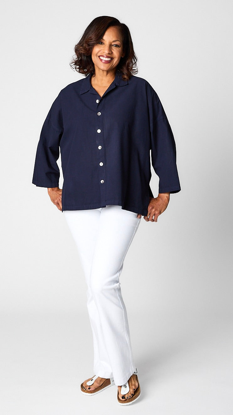 Model wearing indigo button-up top with relaxed hemline and 3/4 sleeves over white bootcut jeans and white sandals.
