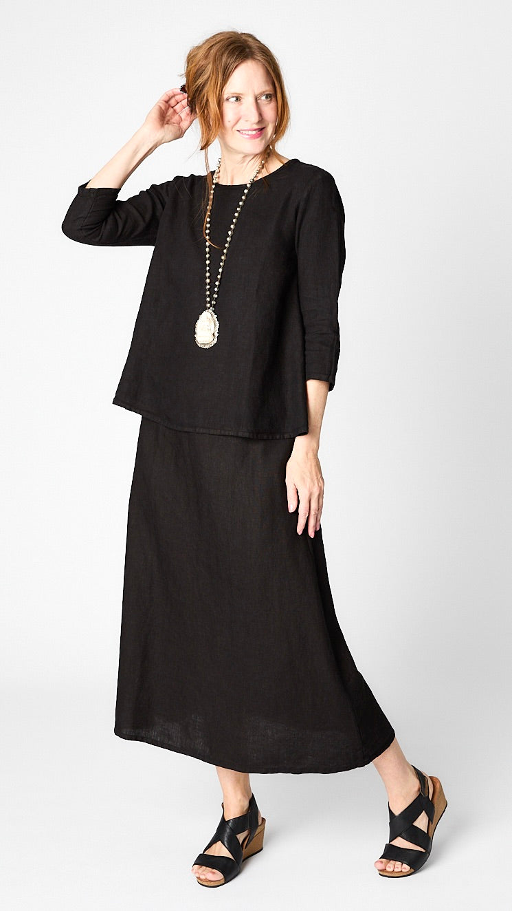 Model wearing black linen 3/4 sleeve shirt with A-line silhouette, black A-Line Linen skirt, bone pendant necklace, and leather sandals.