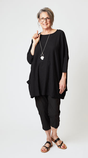 Model wearing oversized black cotton-linen jersey tunic with black cropped, tapered poplin cotton pant and black leather sandals.
