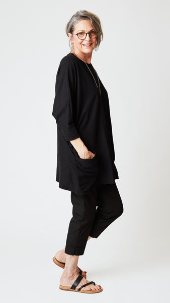 Model wearing oversized black cotton-linen jersey tunic with black cropped, tapered poplin cotton pant and black leather sandals.