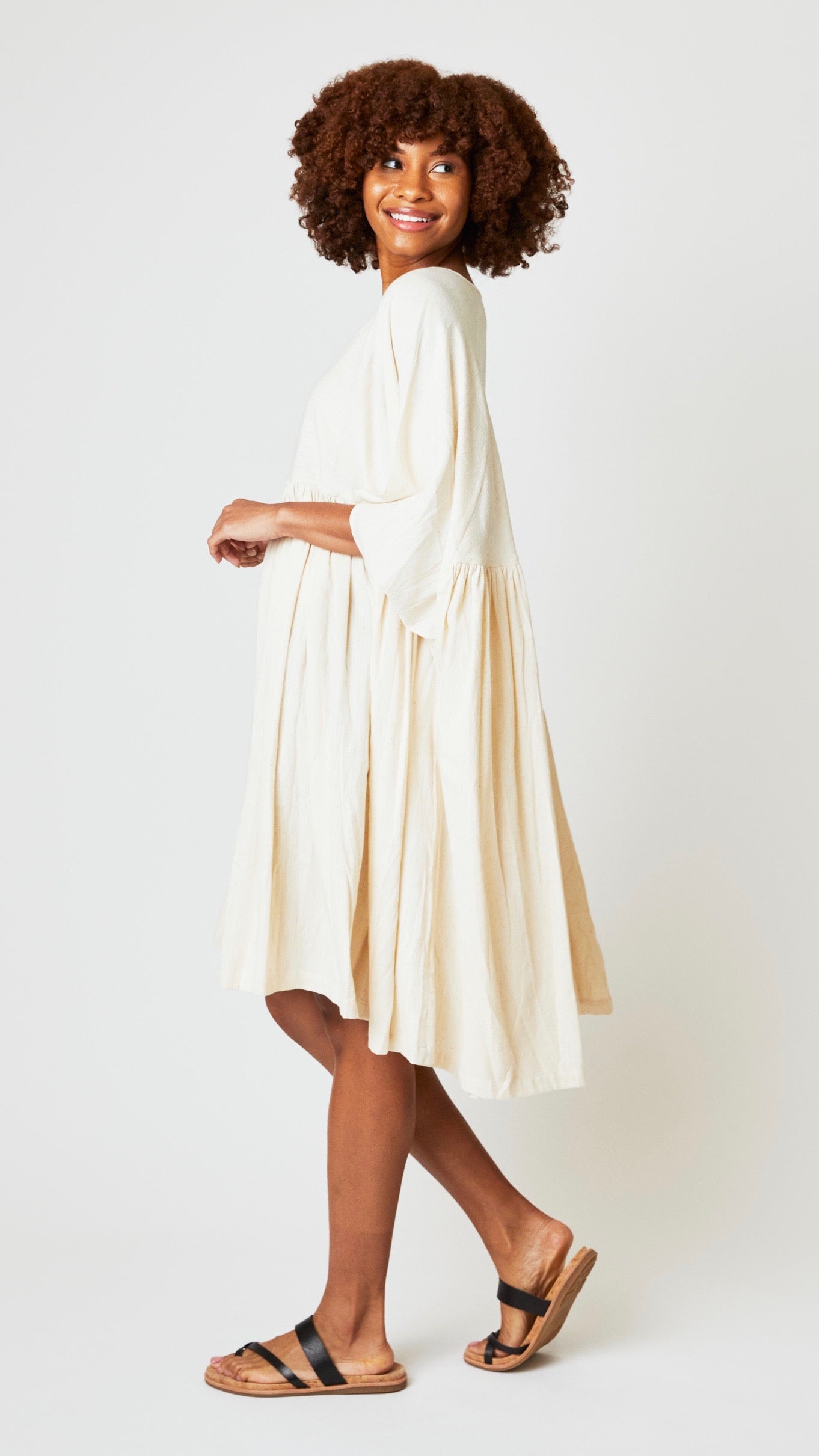 Model wearing oversized natural cotton dress with raglan sleeves and waist-gathered skirt, and black leather sandals.