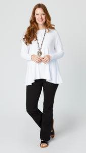 Model wearing white jersey long sleeve top with hip length flare and round neckline, black bootcut jeans, and black leather sandals.