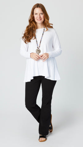 Model wearing white jersey long sleeve top with hip length flare and round neckline, black bootcut jeans, and black leather sandals.
